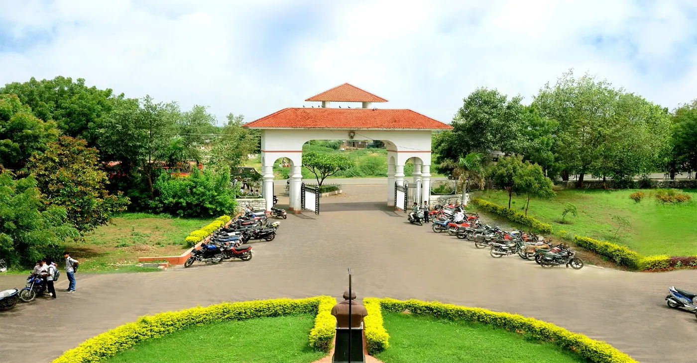 The arched entrance gate of the campus, with a garden roundabout and a bust in the foreground