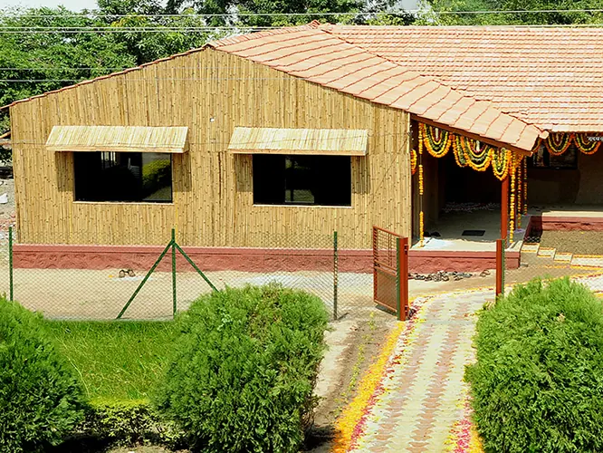 A thatched hut-style building with bamboo walls, the Mahatma Gandhi Adhyayan Kendra, at the end of a garden path